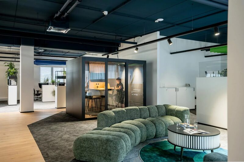 Lounge mit grünem Sofa und einer gläsernen Telefonbox im offenen Arbeitsbereich von Innpuls.